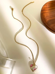 Detail shot of a golden heart necklace with pink enamel on a soft aesthetic background