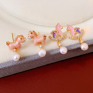 Macro shot of cute pink horse earrings with pearls and zircon stones on a gray display