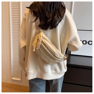 Detail view of cream canvas chest bag with embossed lettering and braided zipper pull