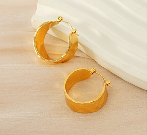 Détail de boucles d'oreilles dorées texturées sur un fond esthétique crème et blanc