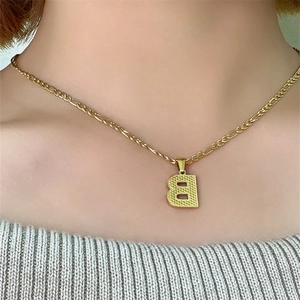 Dettaglio della collana con ciondolo a lettera B dorata e catena Figaro su una modella