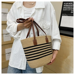 Dettaglio borsa tote in paglia intrecciata a righe nere con manici in pelle marrone