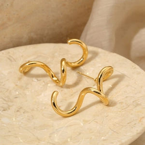 Elegant gold spiral earrings with wavy metal design on marble tray background