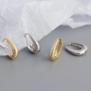 Detail of twisted croissant huggie hoop earrings in gold and silver finish