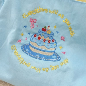 Macro detail of the blue canvas tote bag showing cake embroidery and fabric texture