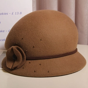 Dettaglio di un cappello cloche in lana marrone con fiore e perline dorate