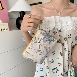 Detailed close-up of floral fabric makeup bag with yellow zipper held by a hand