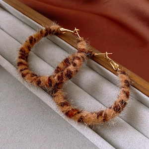 Macro detail of leopard print plush hoop earrings on a velvet gray tray