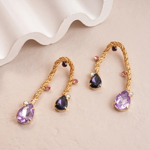 Macro view of gold woven metal earrings with purple and pink teardrop crystals