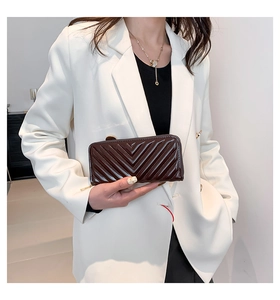 Detail of dark brown quilted patent leather purse with gold zipper held by a model