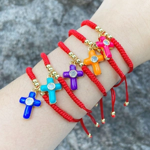 Detail of red braided bracelets with colorful enamel cross pendants and zircon stones