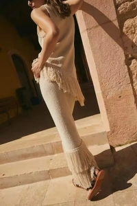 Dettaglio del top smanicato in maglia beige e pantaloni con lunghe nappe decorative