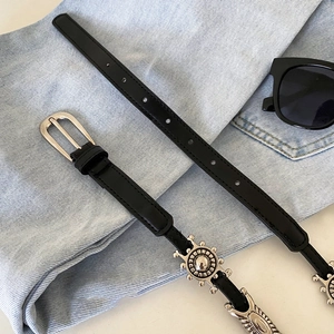 Detail of vintage black leather belt with silver sun wheel buckle on blue denim fabric