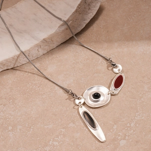 Gros plan du collier argenté asymétrique avec pendentifs géométriques en émail noir et rouge