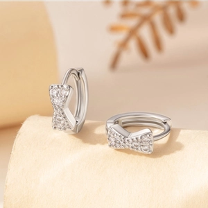 Silver bow-shaped hoop earrings with sparkling cubic zirconia on a soft beige background