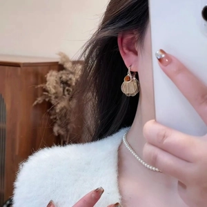 Detailed view of golden ginkgo leaf earrings with amber gemstone on a white faux fur coat