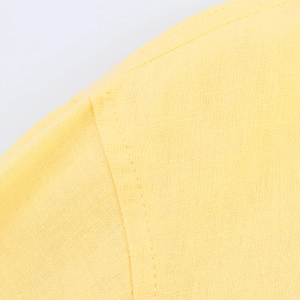 Detailed close-up of yellow cotton linen fabric texture and double-stitched shoulder seams