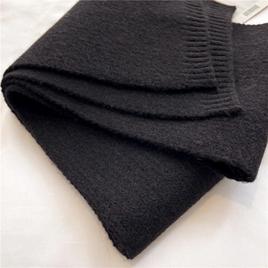 Detailed macro shot of a black knitted scarf featuring soft plush texture and ribbed edges