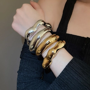 Close-up of stacked gold and silver irregular liquid metal wave bangles on a wrist