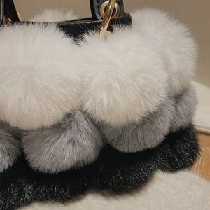 Detail of plush tricolor faux fur balls on handbag with elegant gold metal ring handle