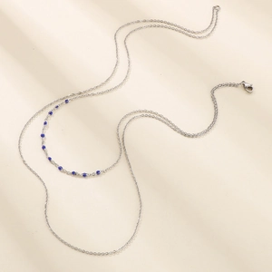 Collier double couche en acier inoxydable avec perles bleues sur fond beige chaleureux