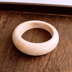 Dettaglio del bracciale largo in resina crema con trama marmorea marrone su legno scuro