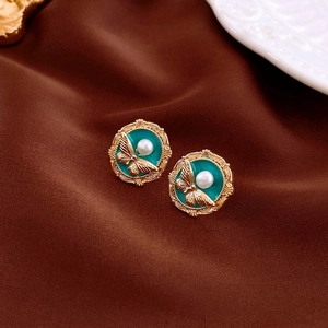 Close-up of vintage gold earrings with green enamel and white pearl butterfly relief