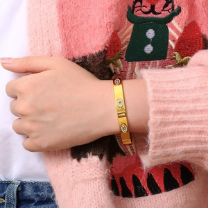 Detail of gold evil eye bangle with blue stones and crystals worn over a pink sweater