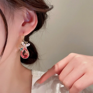 Détail de la boucle d'oreille dorée avec gemme goutte rouge et papillon en zircone