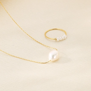 Detail shot of white freshwater pearl necklace and ring set on beige satin fabric