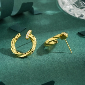 Golden spiral textured stud earrings with sparkling cubic zirconia on a green background