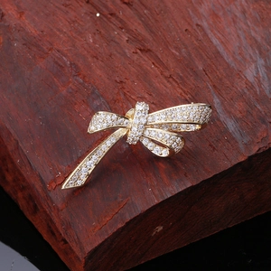 Detailed view of a gold bow brooch with inlaid zircons on a dark wood background