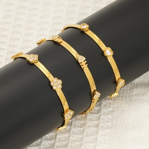 Trois bracelets chaîne serpent dorés avec breloques cœur et fleurs sur présentoir noir