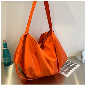 Detail of a vibrant orange large capacity pleated tote bag on a metallic surface