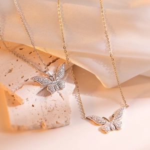 Elegant gold and silver butterfly pendant necklaces with crystals on textured stone