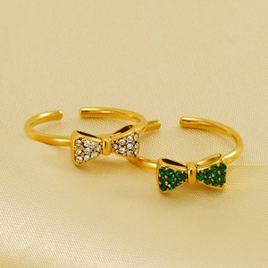 Macro view of gold bow rings with white and green rhinestones on elegant silk background
