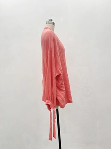 Side view of coral orange oversized shirt featuring textured pleated fabric and tie cuffs