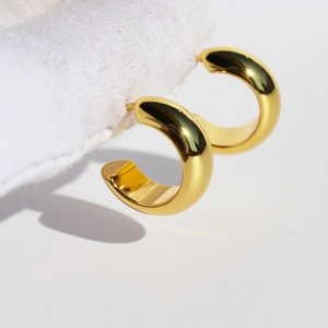 Chunky gold-plated C-shaped hoop earrings with a high-polish finish on a white fabric