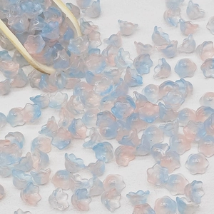 Detailed macro of gradient blue and pink lily of the valley glass beads in wooden spoon