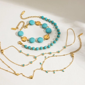 Golden stainless steel jewelry set with turquoise beads and heart charms on white textured background