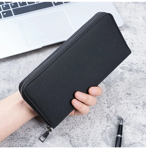 Close-up of black canvas business wallet with durable metal zipper and laptop background