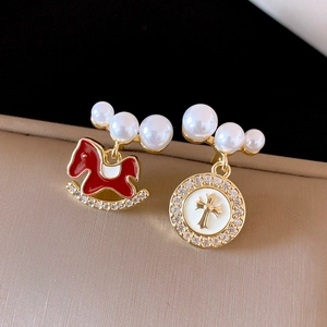 Detail of asymmetrical earrings with red rocking horse and golden cross charm