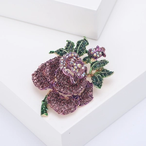 Elegant gold rose brooch with sparkling purple and green rhinestones on white display
