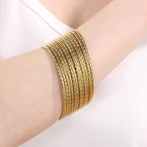 Detail of gold stacked twisted rope bracelets on wrist showing fine metal textures