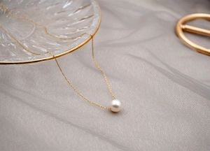 Close-up of a delicate single white pearl pendant on a thin gold chain necklace