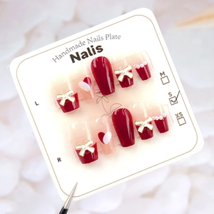 Detail of burgundy press-on nails featuring white 3D bows and pearl heart accents