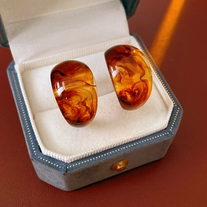 Macro detail of amber C-shaped earrings with marble texture in a blue velvet jewelry box