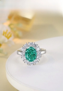 Macro shot of oval green emerald ring with silver diamond halo on display stand