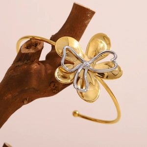 Detail of 18K gold plated flower bangle with two-tone heart detail on wooden branch
