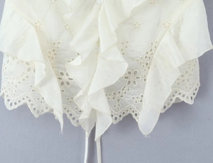 Close-up of white cotton top with ruffles, hollow embroidery, and drawstring tie hem